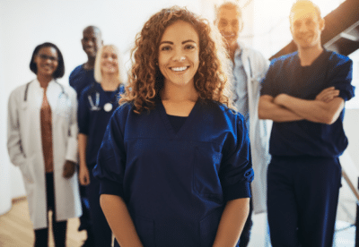 Smiling young female doctor standing in a hospital corridor with a diverse group of medical staff standing behind her