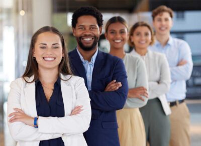 Five diverse people stand in a row smiling with their arms crossed
