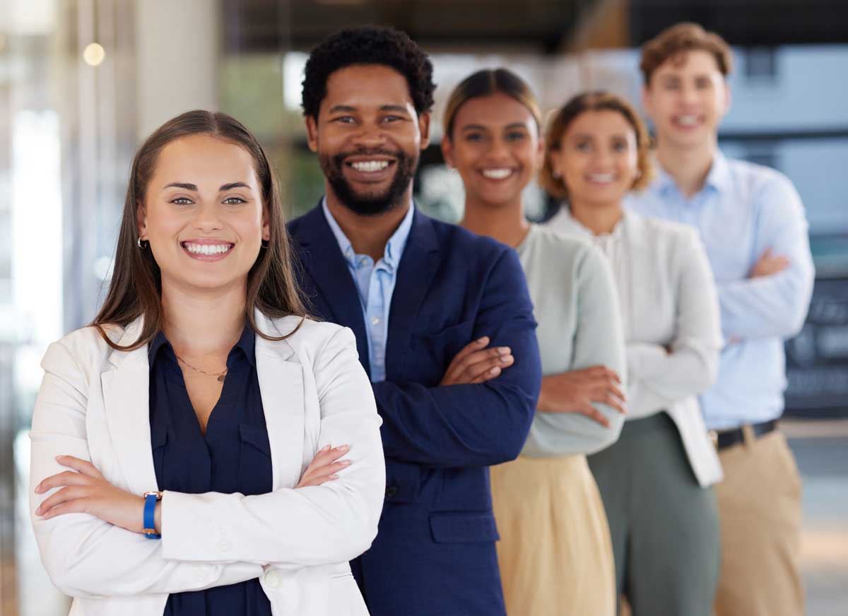 Five diverse people stand in a row smiling with their arms crossed