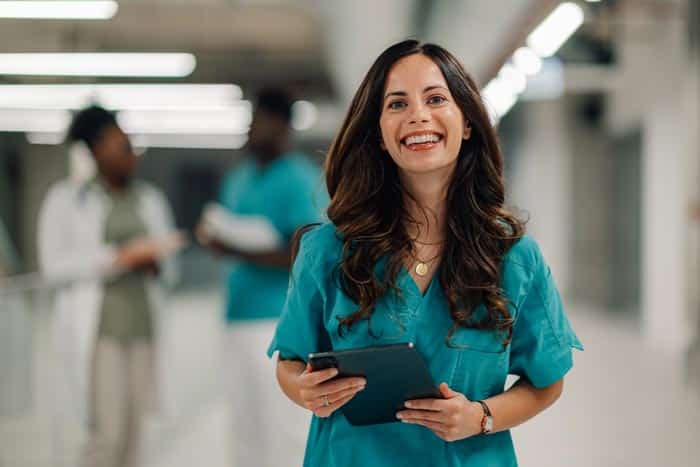 A medical professional wearing teal scrubs smiles broadly